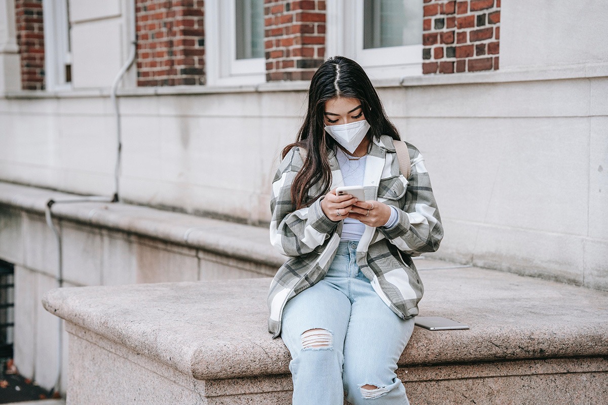 Female student with a mask on sitting on a cement wall.