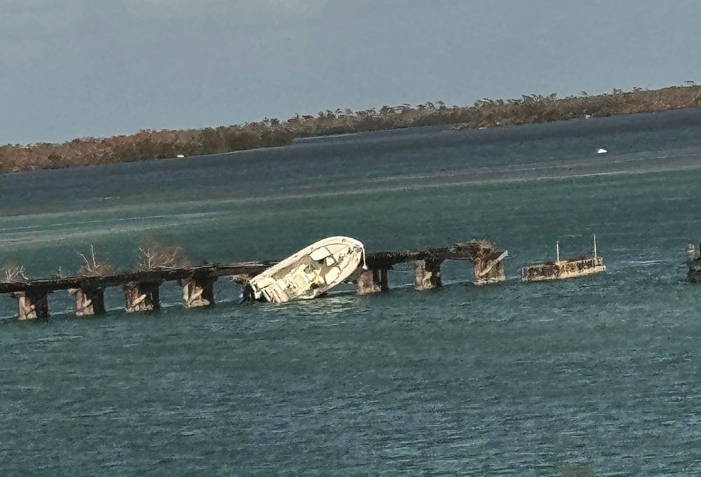 Small white boat capsized against a pier after a natural disaster.