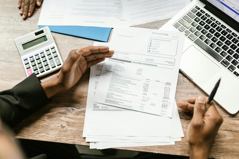 A stack of papers sitting in front of someone, next to a laptop and calculator.