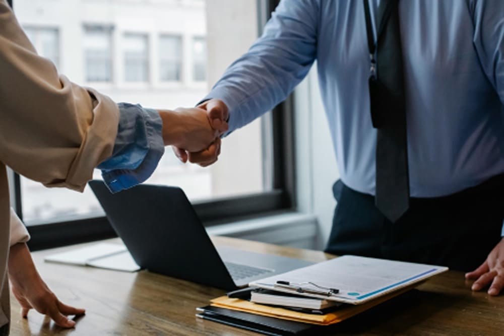 Two people shaking hands over a wooden desk after discussing mitigation projects.