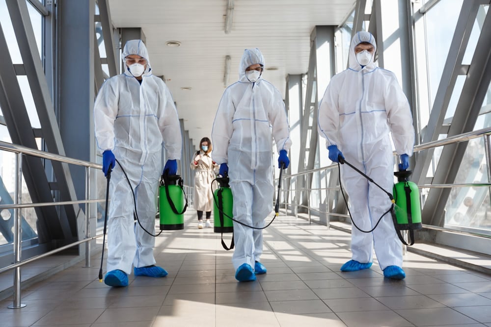 Three people in ppe with disinfecting materials.
