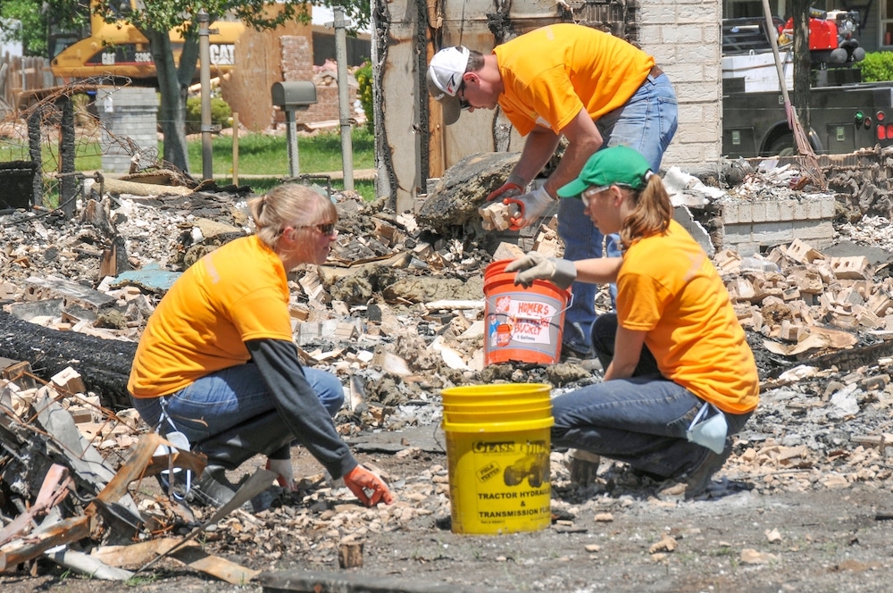 Volunteers in orange shirts sorting through debris from a recent disaster.